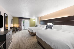 Ein Hotelzimmer mit zwei Betten, einem Schreibtisch, einem Stuhl, einem Fernseher und einem Badezimmer mit Dusche und Toilette.