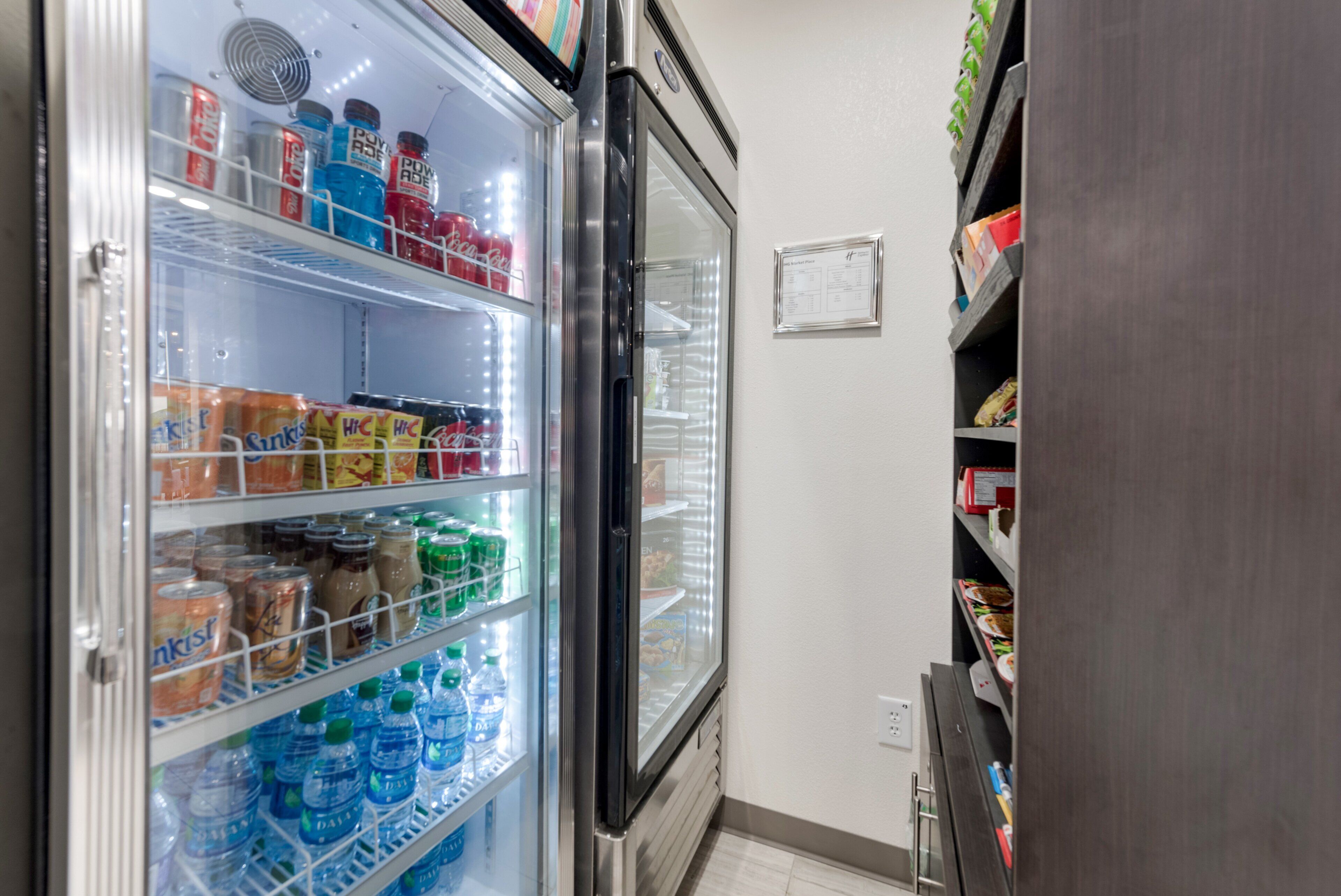 Un expositor refrigerado con bebidas y aperitivos, una puerta de congelador y un cartel en la pared.