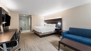 A hotel room with a bed, a blue sofa, a desk with a chair, and a TV.