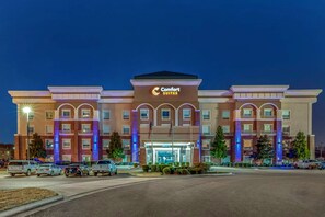 A Comfort Suites hotel with a prominent entrance, multiple flags, and a parking lot with several cars.