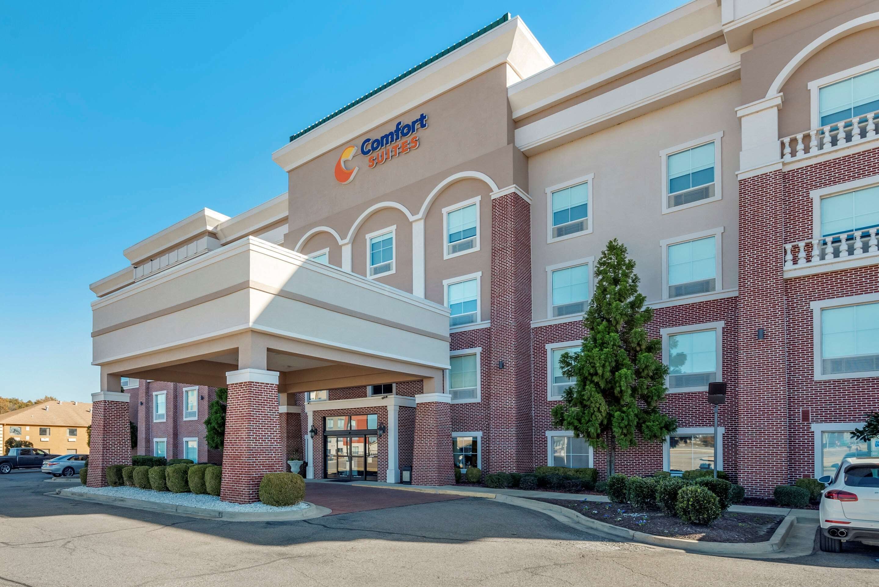 A Comfort Suites hotel with a brick facade, a covered entrance, and a clear blue sky.
