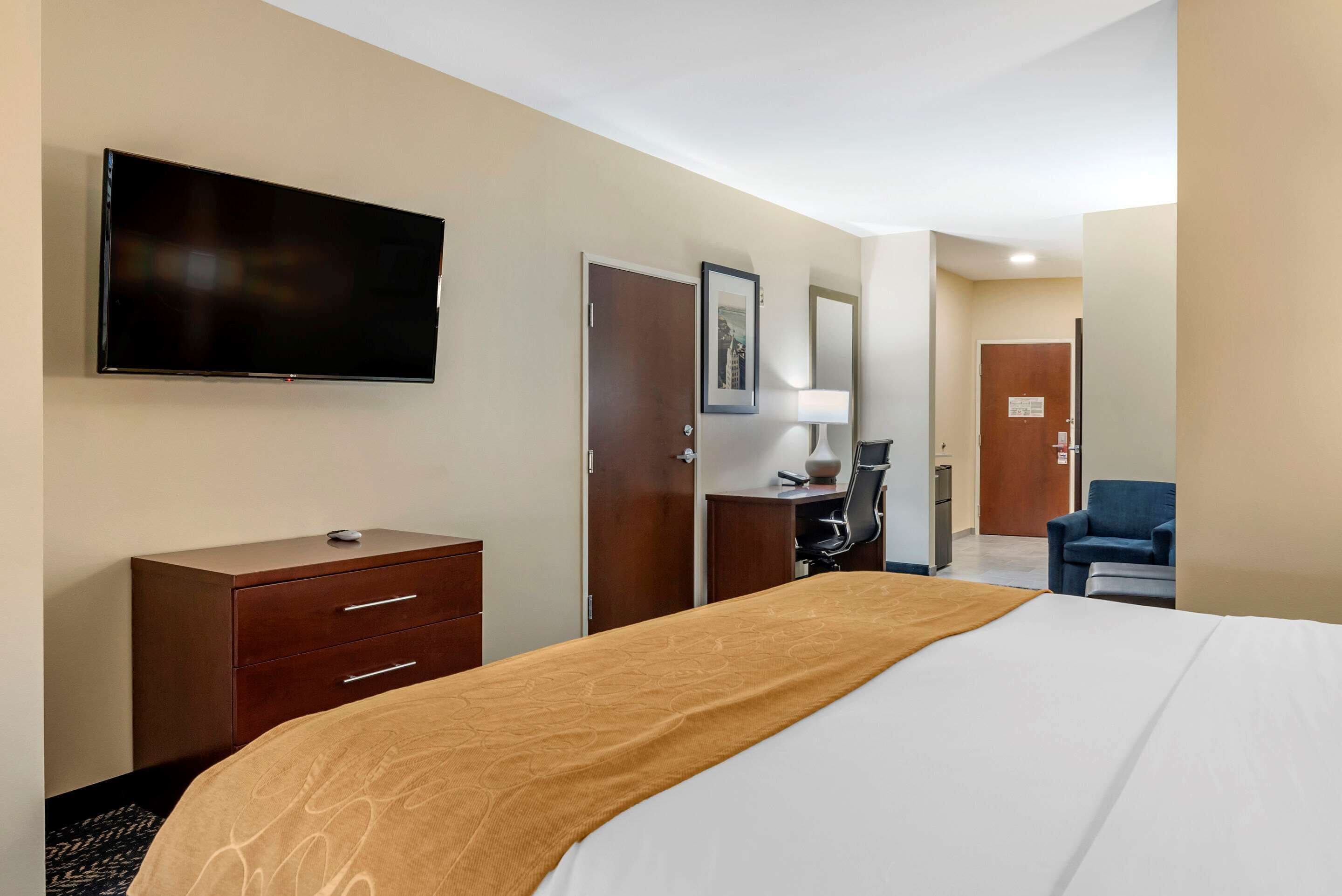 Une chambre d’hôtel avec un lit, un téléviseur fixé au mur, un bureau avec une chaise et une porte.