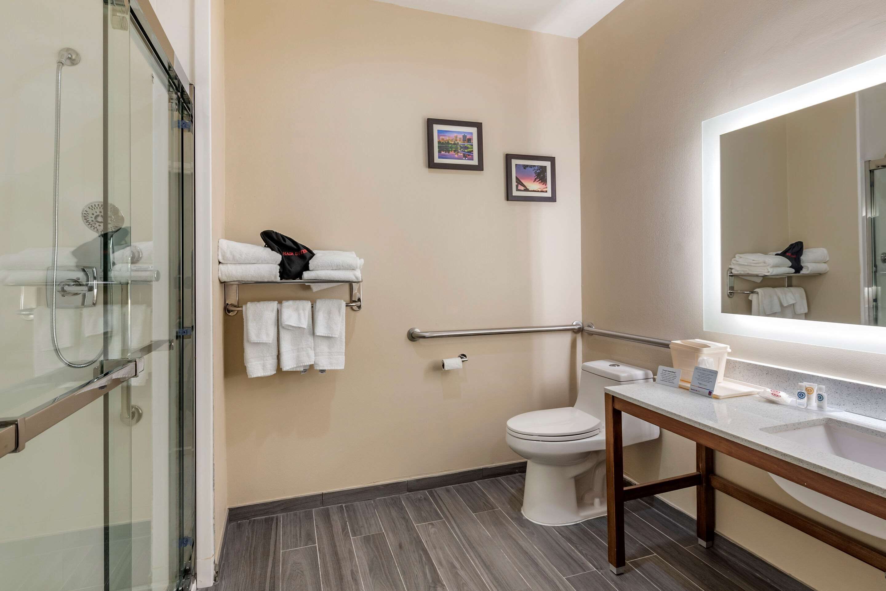 Un baño moderno con cabina de ducha de vidrio, inodoro, tocador con lavamanos y dos cuadros en la pared.