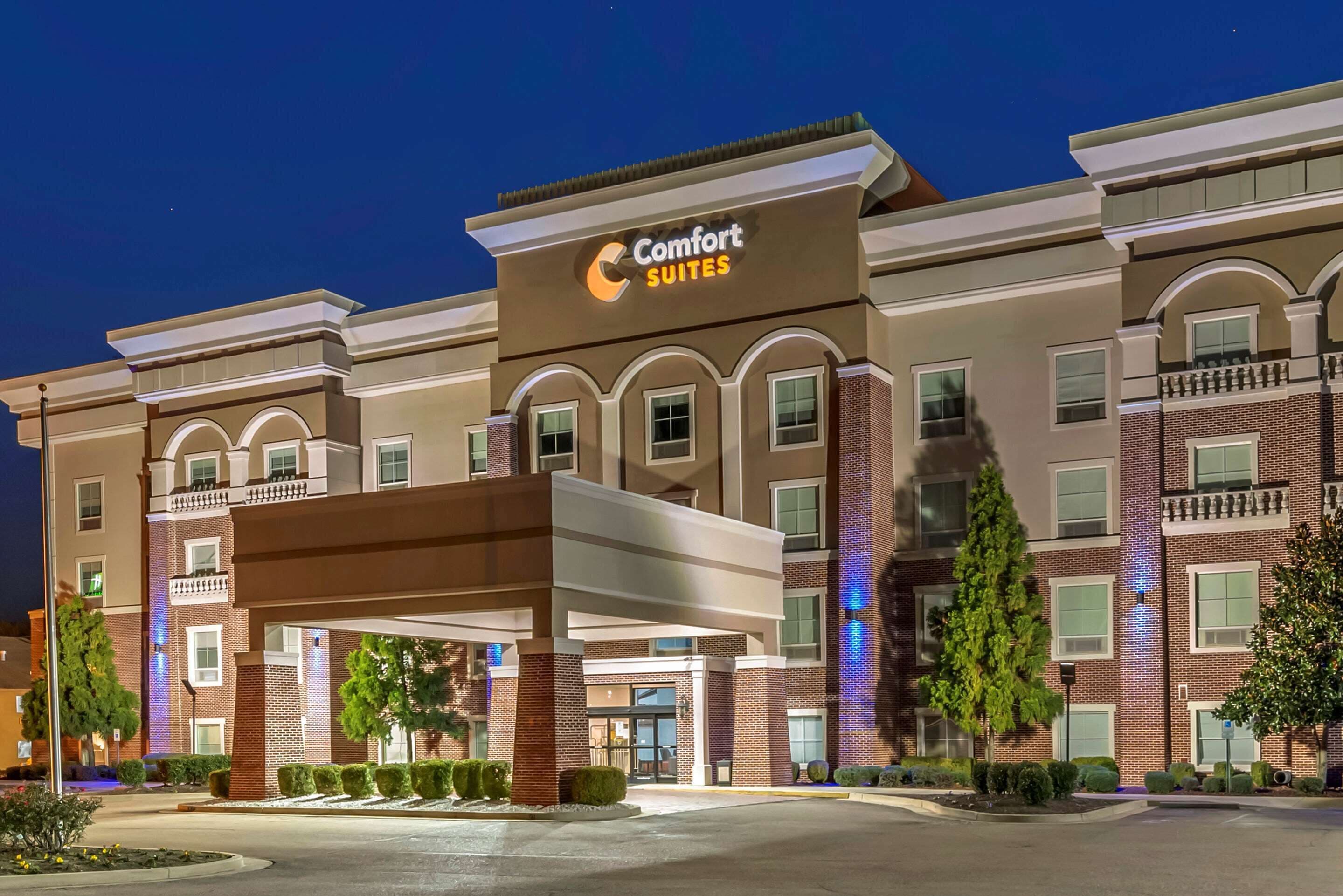 Um hotel Comfort Suites com fachada moderna, várias varandas e uma entrada bem iluminada.