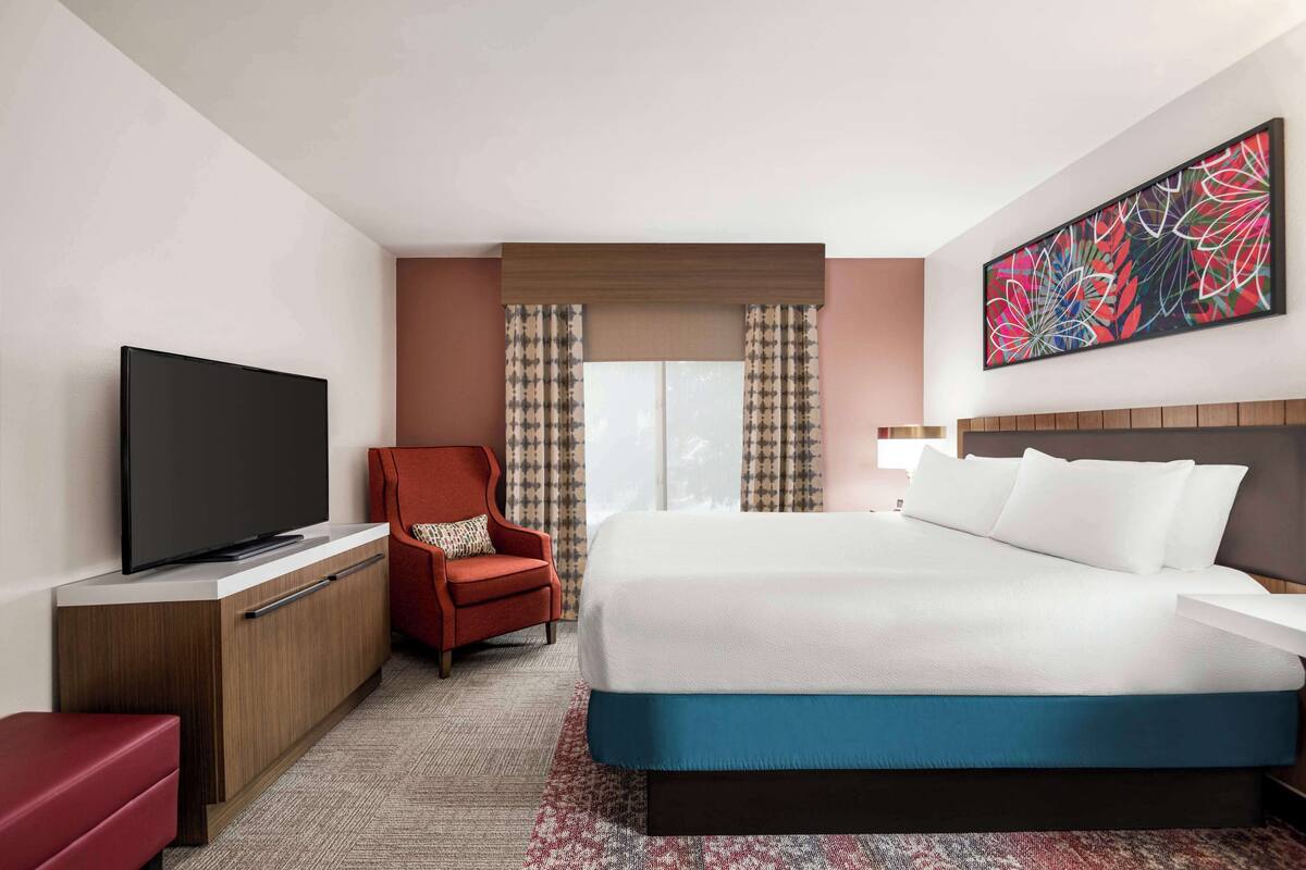 Une chambre d’hôtel avec un grand lit, une télévision, un fauteuil rouge et un élément décoratif mural.
