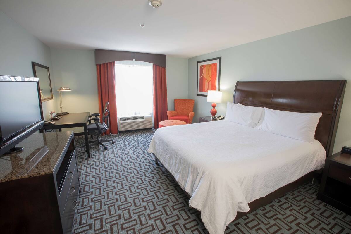 Une chambre d’hôtel avec un lit, un bureau, une chaise, une télévision et une fenêtre avec des rideaux.