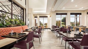 Un restaurant moderne doté de hauts plafonds, de grandes fenêtres et proposant différents types de sièges, notamment des banquettes et des tables.