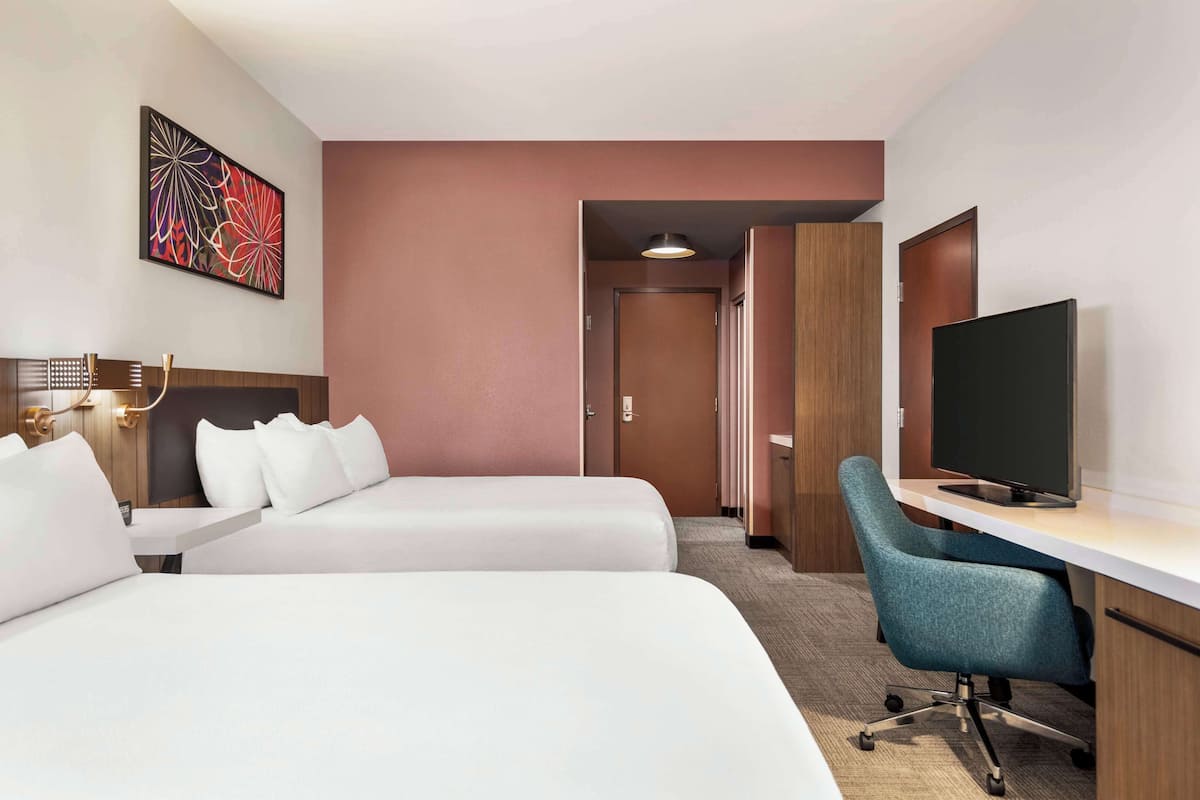 Une chambre d’hôtel avec deux lits, un bureau avec une chaise, une télévision et un tableau au mur.