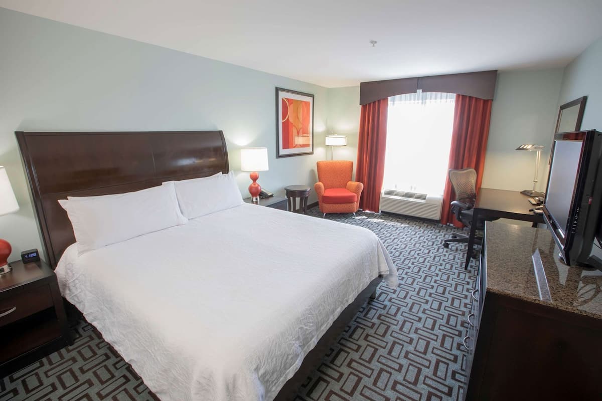 Une chambre d’hôtel avec un grand lit, un bureau, une chaise, une télévision et une fenêtre avec des rideaux.