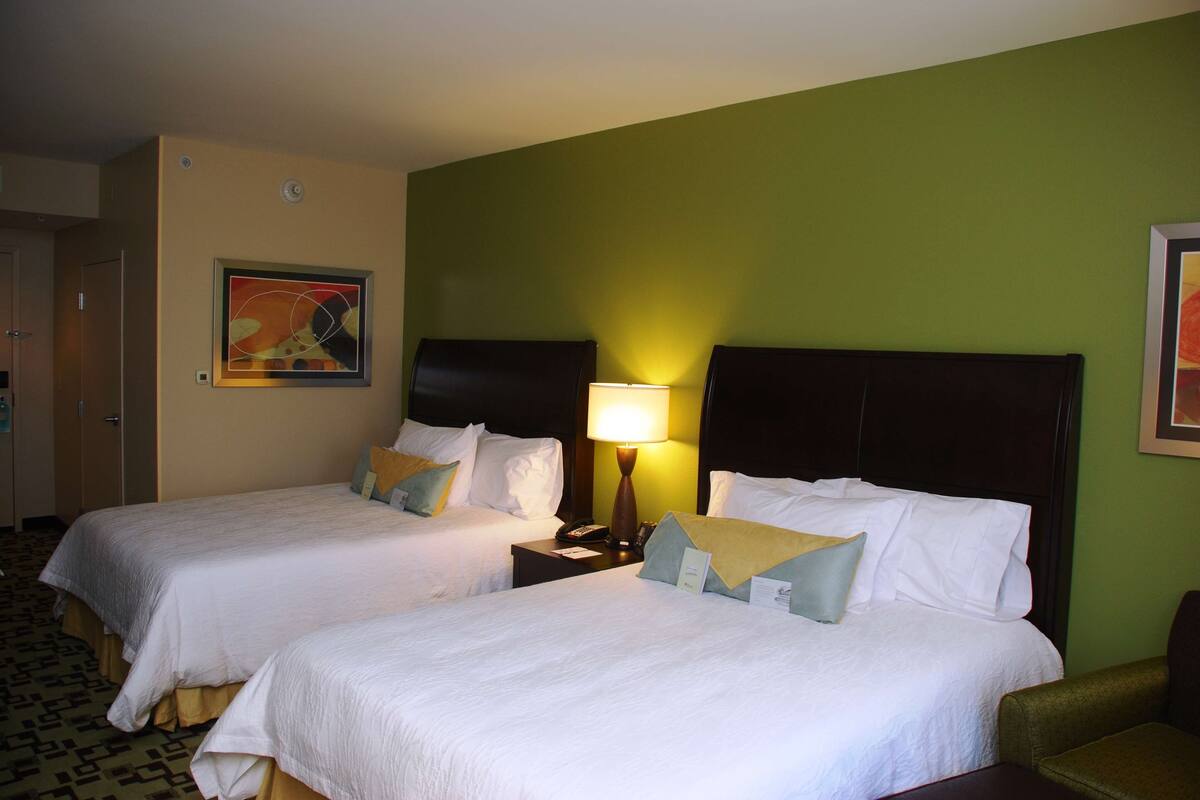 Habitación de hotel con dos camas, una mesita de noche con lámpara y un cuadro en la pared.