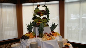 Presentación de frutas y quesos con una bandeja escalonada de fruta, rodeada de diversos quesos y frutas sobre una mesa.