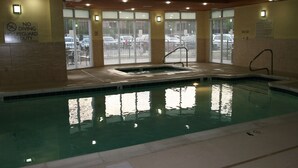 Una piscina interior con un cartel de prohibido bucear, un anuncio de presencia de salvavidas y vistas a coches estacionados a través de las ventanas.