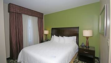Una habitación de hotel con una cama grande, dos mesitas de noche y un ventanal con cortinas.
