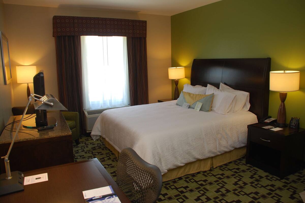 Habitación de hotel con una cama grande, dos lámparas de noche, un escritorio con lámpara, una silla y una ventana con cortinas.