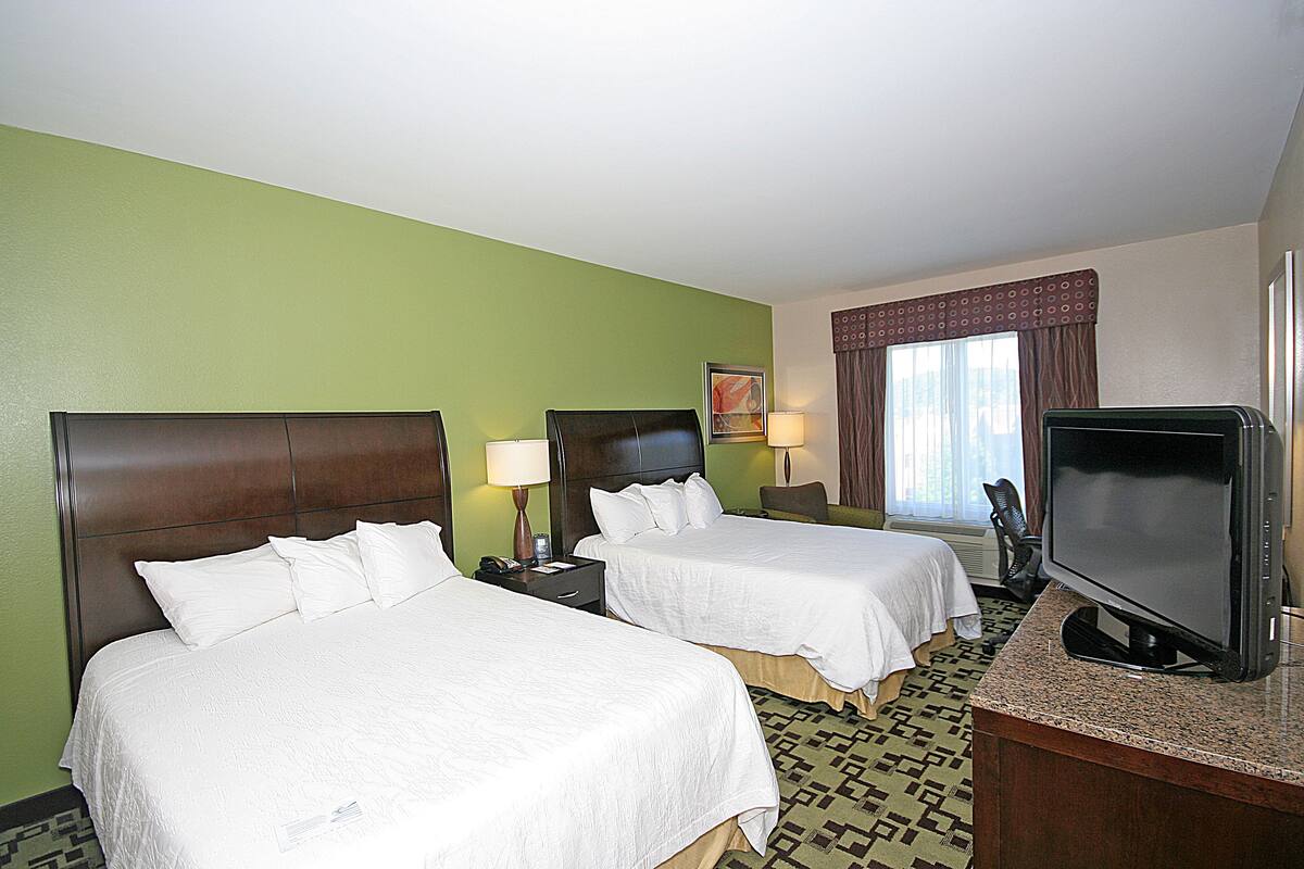 Habitación de hotel con dos camas, televisión y escritorio.