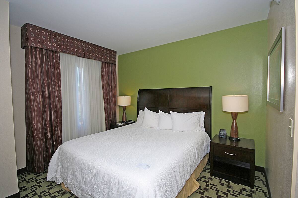 Una habitación de hotel con una cama grande, dos mesitas de noche con lámparas, un suelo estampado y paredes verdes.