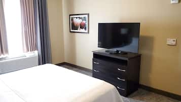 A hotel room with a bed, a TV on a dresser, a framed picture on the wall, and a window with curtains.