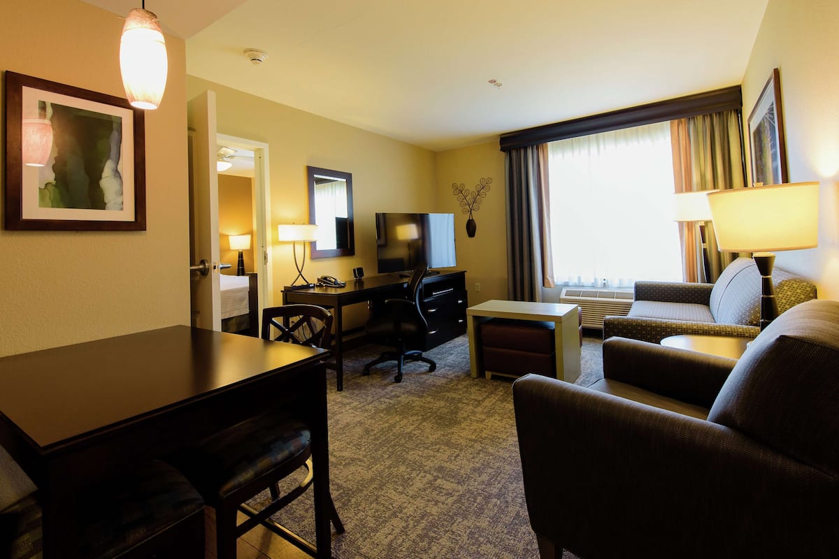A hotel room with a dining table, a TV, a sofa, and a desk.
