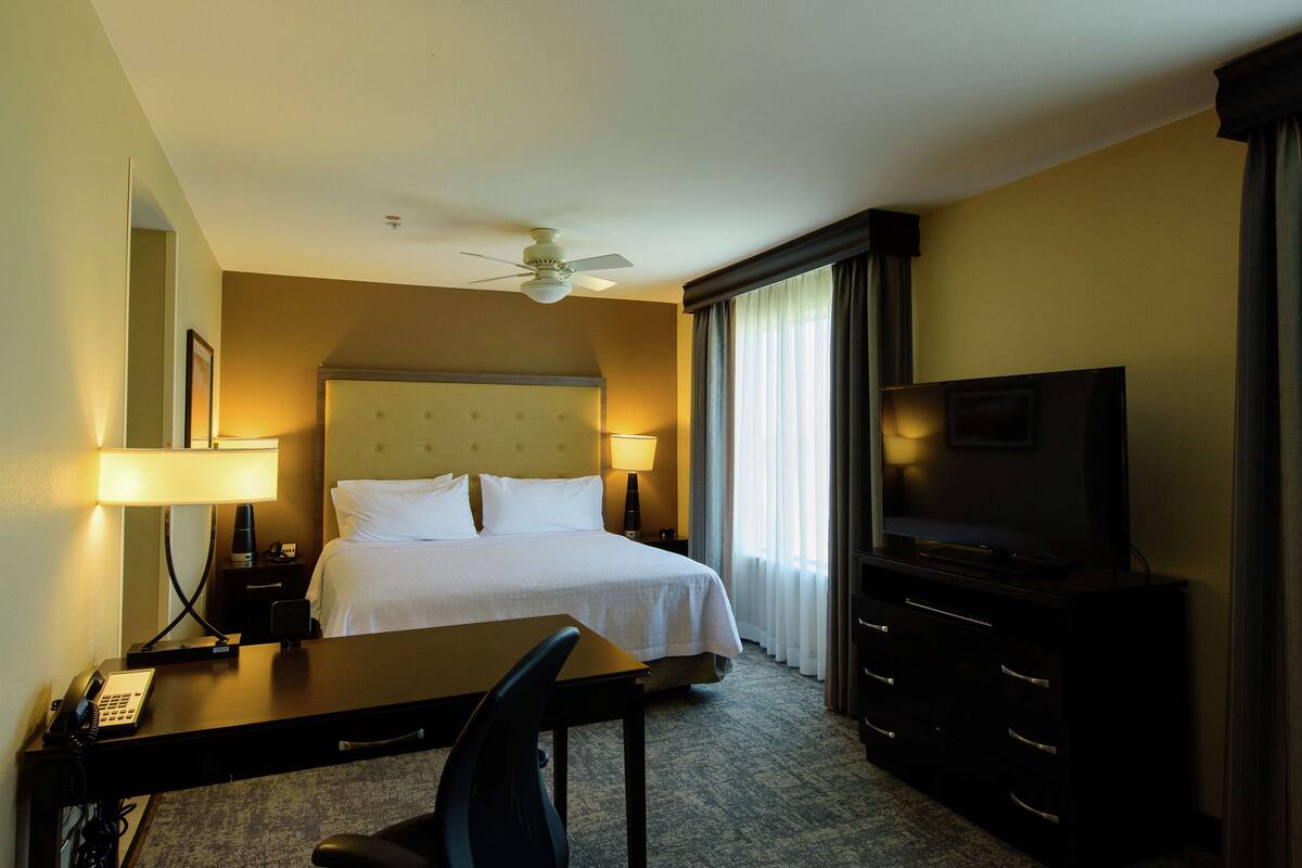 A hotel room with a bed, a desk with a telephone, a television, and a ceiling fan.