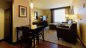Een hotelkamer met een eettafel, stoelen, een bank, een televisie en een koelkast.