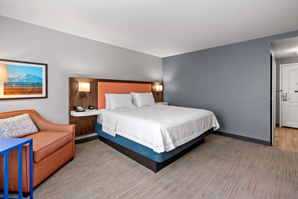A hotel room with a bed, a nightstand, a desk, a chair, and a painting on the wall.