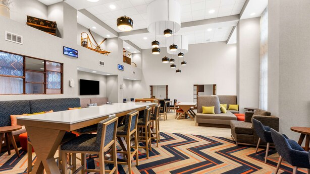 A spacious hotel lobby with a long communal table, multiple seating areas, and a modern chandelier. - Hampton Inn & Suites Fairbanks (Fairbanks)