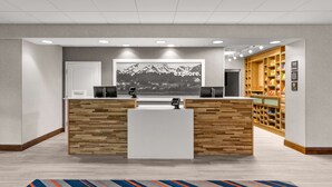 A reception desk with a wooden design, a large framed picture on the wall, and a storage area with shelves. - Hampton Inn & Suites Fairbanks (Fairbanks)