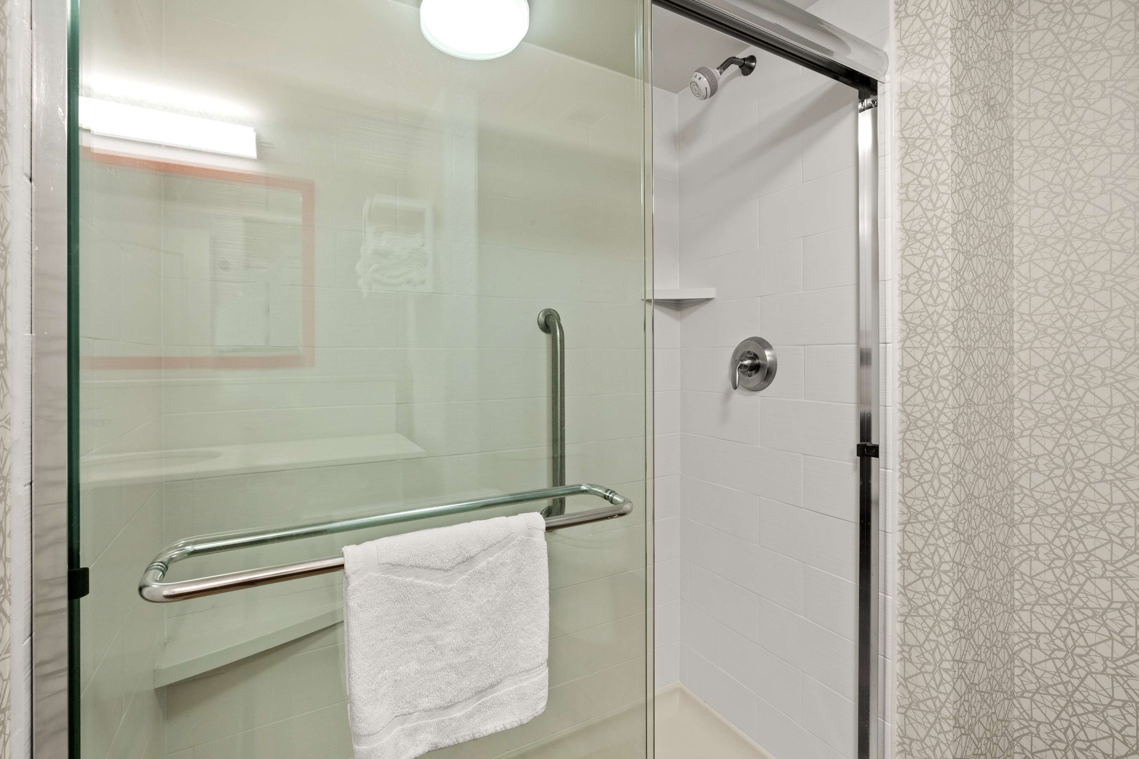 Un baño moderno con cabina de ducha de vidrio, puerta de vidrio y una toalla blanca colgada en un perchero metálico.