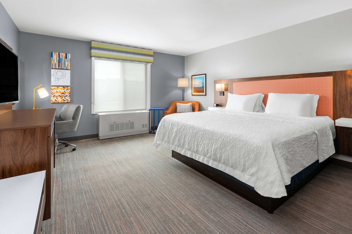 A hotel room with a large bed, a desk, a chair, a TV, and artwork on the walls.