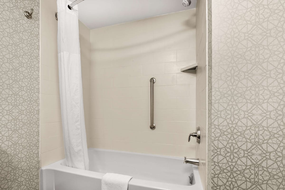 A modern bathroom with a bathtub, a shower curtain, a grab bar, and patterned tiles.