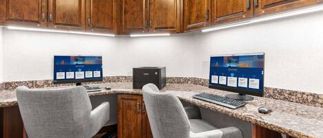 A corner office with two desks, each with a computer and keyboard, wooden cabinets, and a carpeted floor.