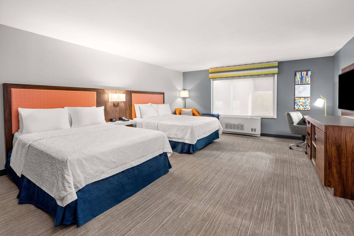 A hotel room with two beds, a desk, a chair, a TV, and a window with a view.