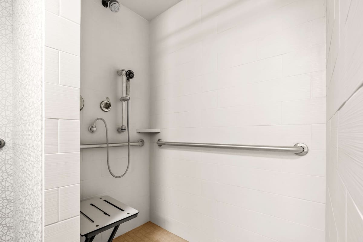 A modern bathroom with white tiled walls, a shower with a handheld showerhead, a grab bar, and a towel rack.
