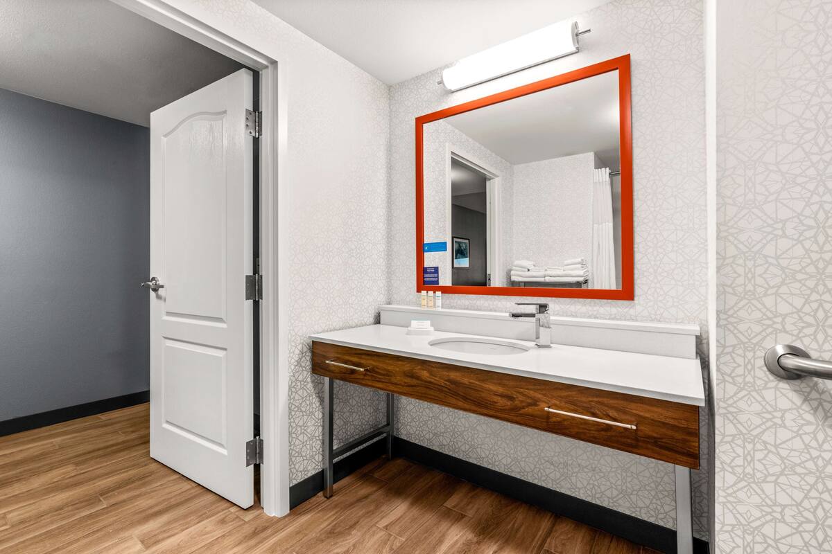 A modern bathroom with a white vanity, a mirror with an orange frame, and patterned wallpaper.