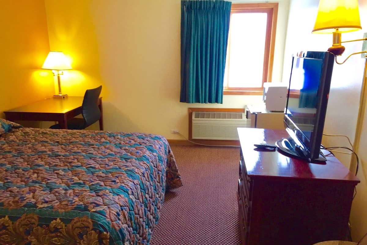 Quarto de hotel com cama, escrivaninha, televisão e ar condicionado.