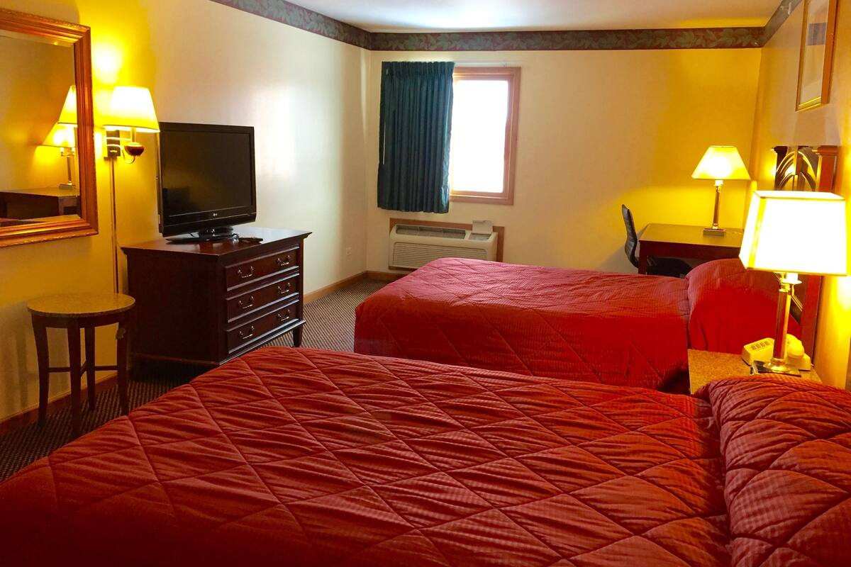 Quarto de hotel com duas camas, uma televisão, uma cômoda e duas luminárias.