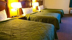 Ein Hotelzimmer mit drei Einzelbetten, jedes mit einer grünen Bettdecke und weißen Kissen. Auf jedem Bett befinden sich zwei Nachttischlampen.