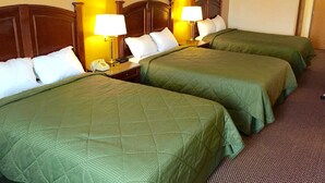 Ein Hotelzimmer mit drei Betten, jedes mit einer grünen Bettdecke und weißen Kissen. Nachttische mit Nachttischlampen und Telefon.