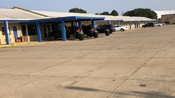 A row of motel rooms with blue awnings and a parking lot with several cars. - Amber Inn Motel Le Mars (Le Mars)