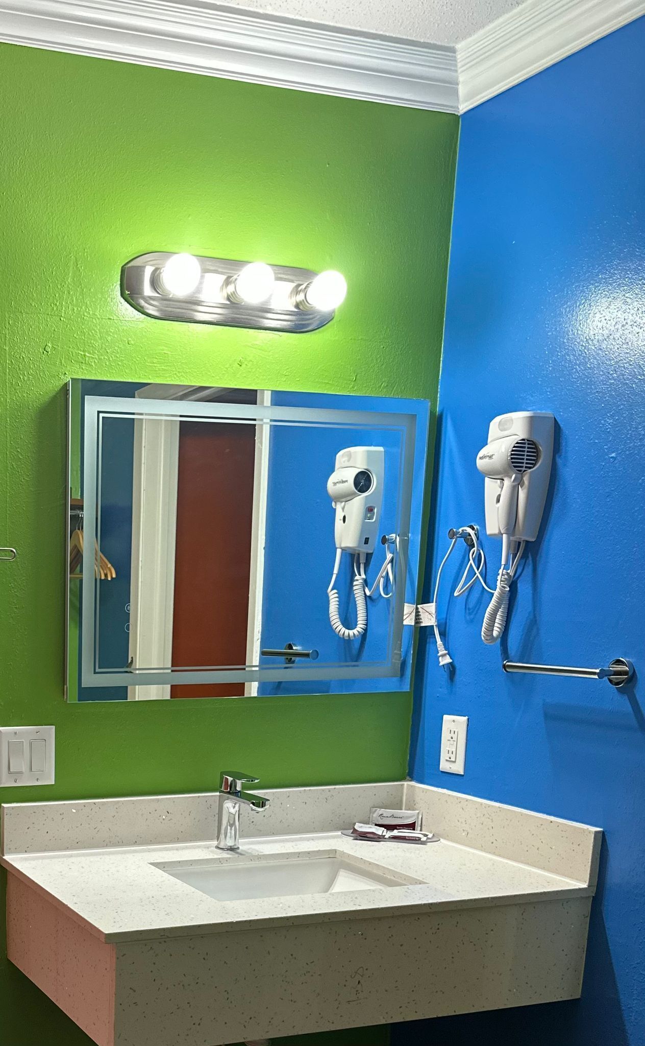 A bathroom with a green wall, a blue wall, a white sink, and a hairdryer mounted on the wall.
