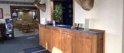 A reception area with a wooden counter, mounted deer heads, a potted plant, and a reception desk.