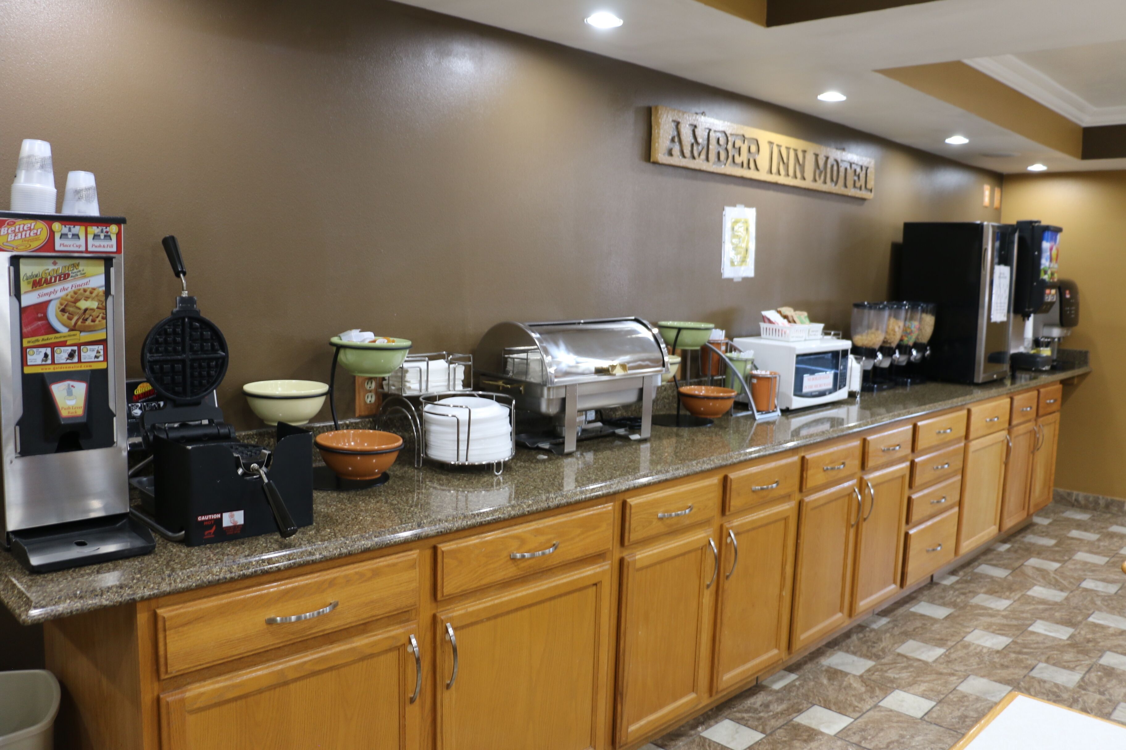 A breakfast bar with a waffle maker, coffee machine, and various bowls and containers.