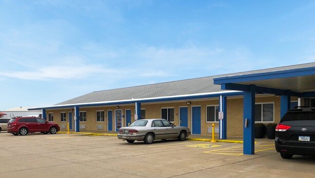 A motel with a parking lot, a covered waiting area, and a building with a blue and beige facade. - Amber Inn Motel Le Mars (Le Mars)