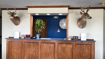 A reception desk with wooden paneling, a clock, and two mounted deer heads above it.