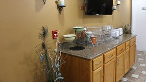 A kitchen with wooden cabinets, a granite countertop, a microwave, a coffee maker, and a television mounted on the wall. - Amber Inn Motel Le Mars (Le Mars)