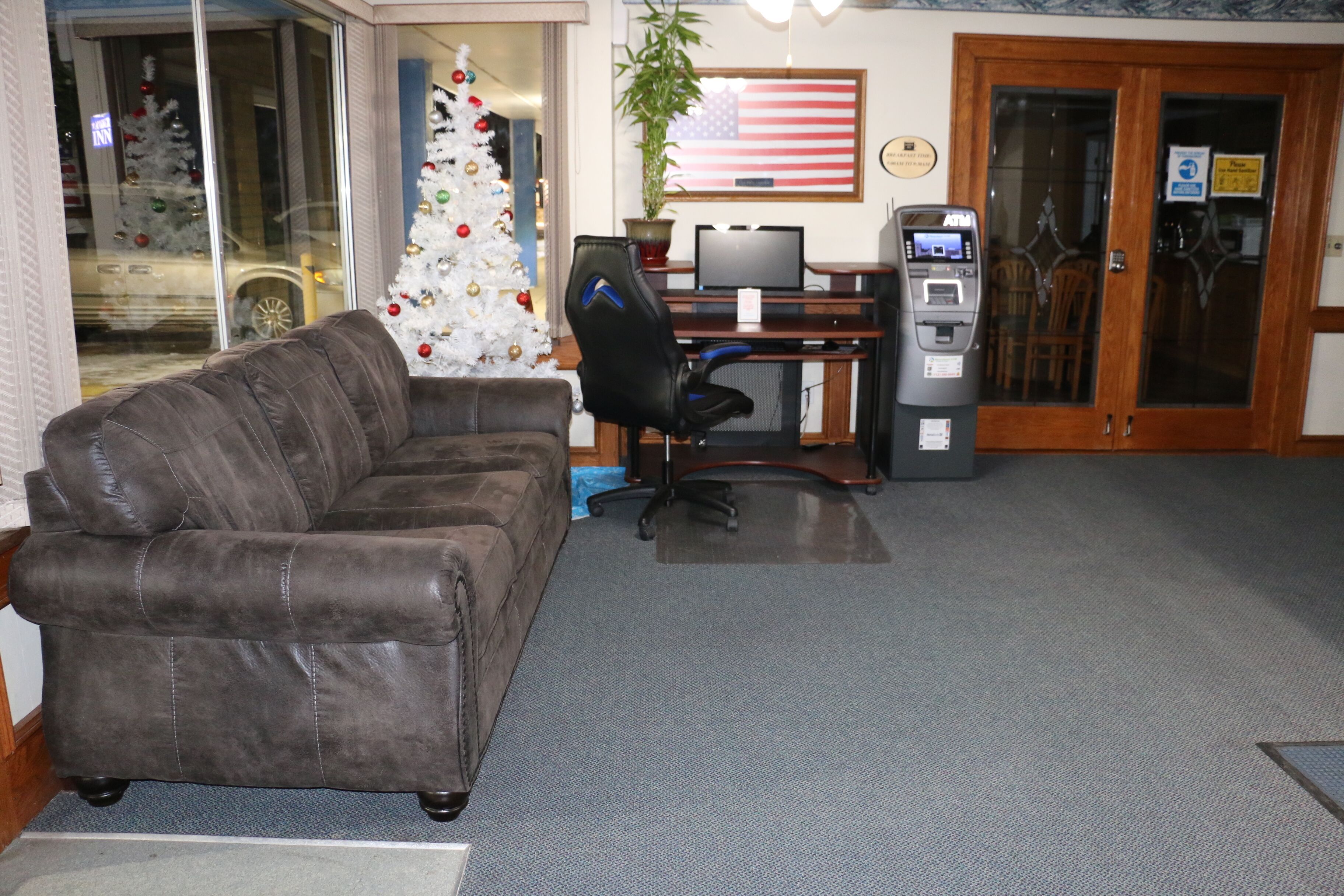 A room with a brown leather sofa, a desk with a computer, an ATM machine, and a Christmas tree.