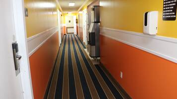A hotel corridor with a striped carpet, a vending machine, and a sign listing amenities like rooms, ice and vending, front desk, restroom, fitness room, and laundry room.