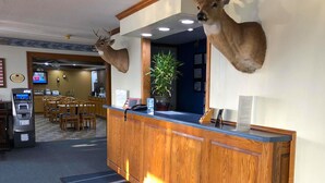 A hotel reception area with a wooden counter, mounted deer heads, a plant, and a TV screen. - Amber Inn Motel Le Mars (Le Mars)