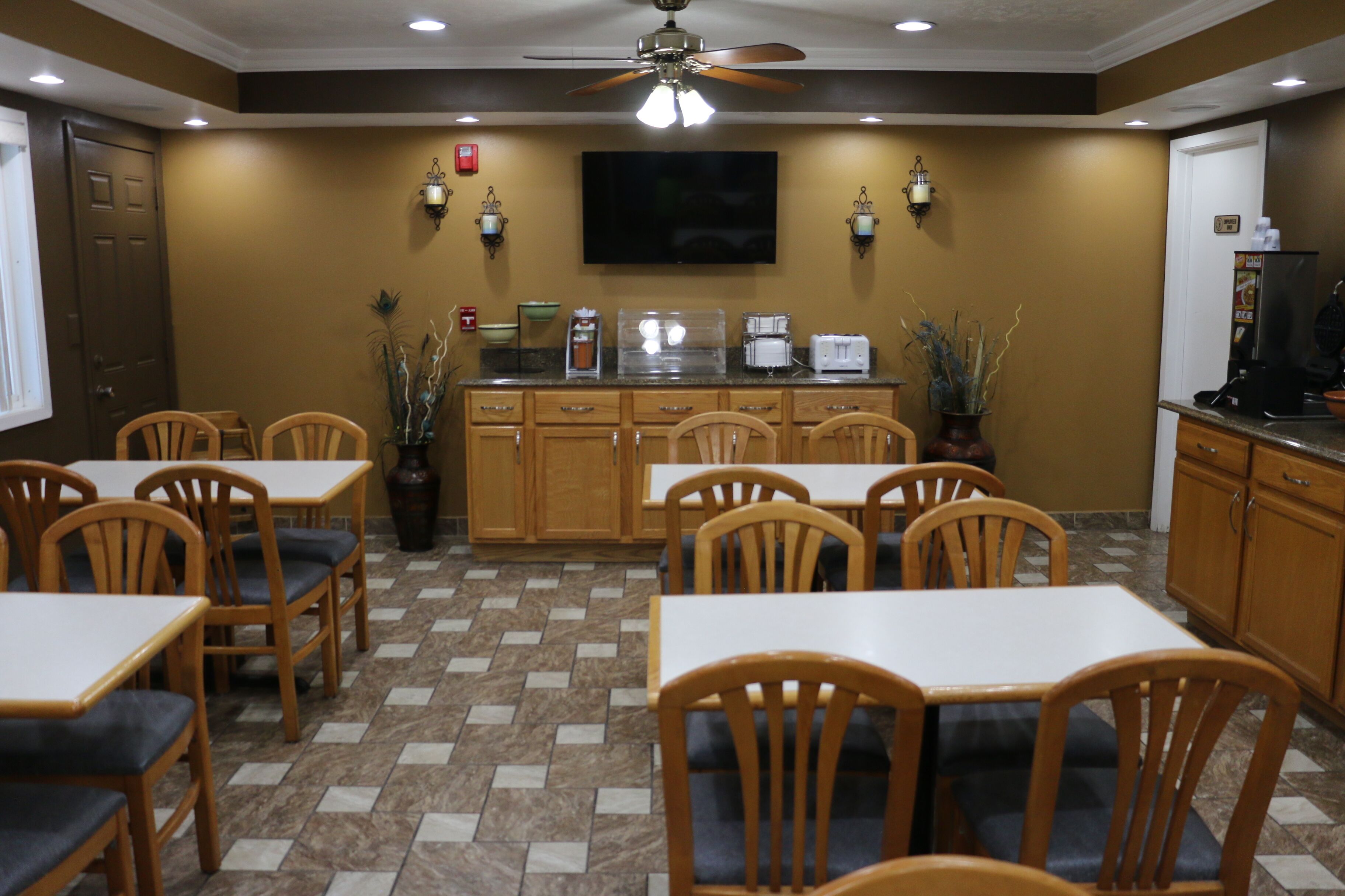 A dining area with wooden tables and chairs, a kitchen counter with appliances, and a ceiling fan.