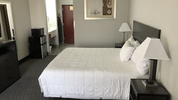 A hotel room with a large bed, a nightstand with a lamp, a dresser, a microwave, and a door leading to a bathroom.